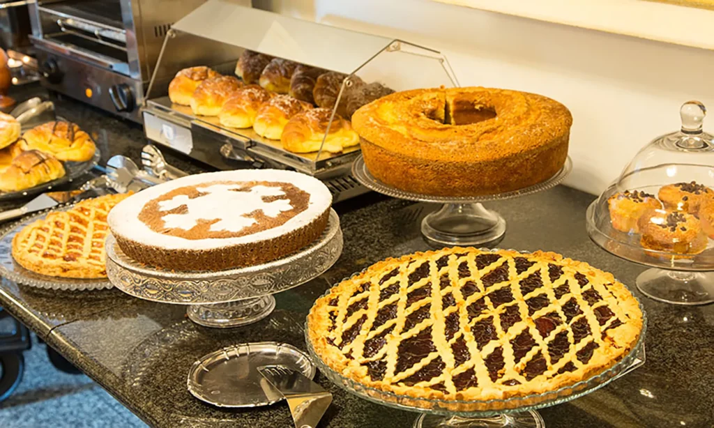 In the picture, a detail of the breakfast buffet of the Hotel Rivoli with some cakes, fruit tarts and various types of croissants.