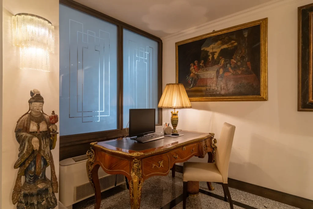 In the picture, the Internet Point of the Hotel Rivoli: we can see a table with a laptop and a lamp- On the right, a painting is hanging on the wall.